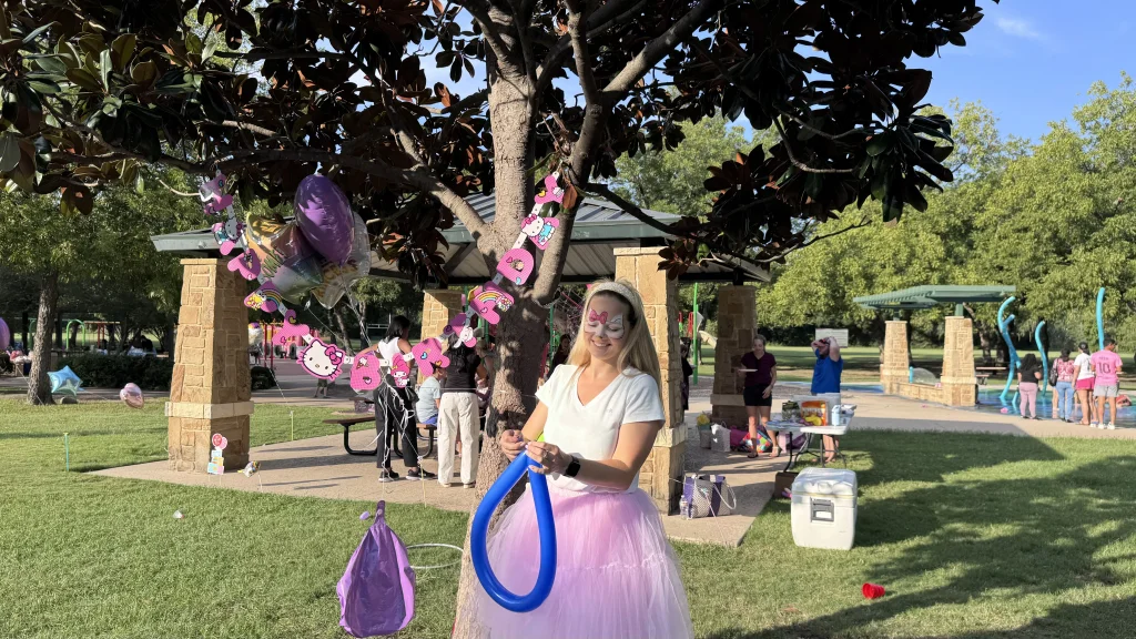Twisting a long blue balloon at a park birthday party